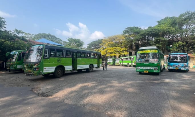A small India bus yard with green public transit buses.
