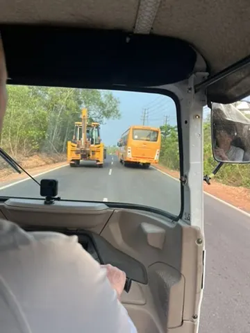 Image from the perspective of driving a rickshaw on a road with large machinery tractors and buses.