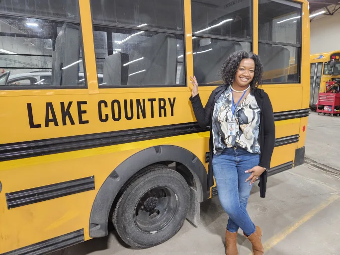 a woman stands in front of a school bus