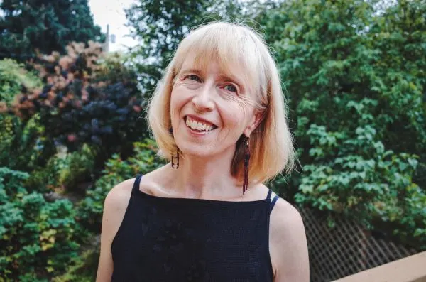 headshot of a woman standing against a green tree lined background
