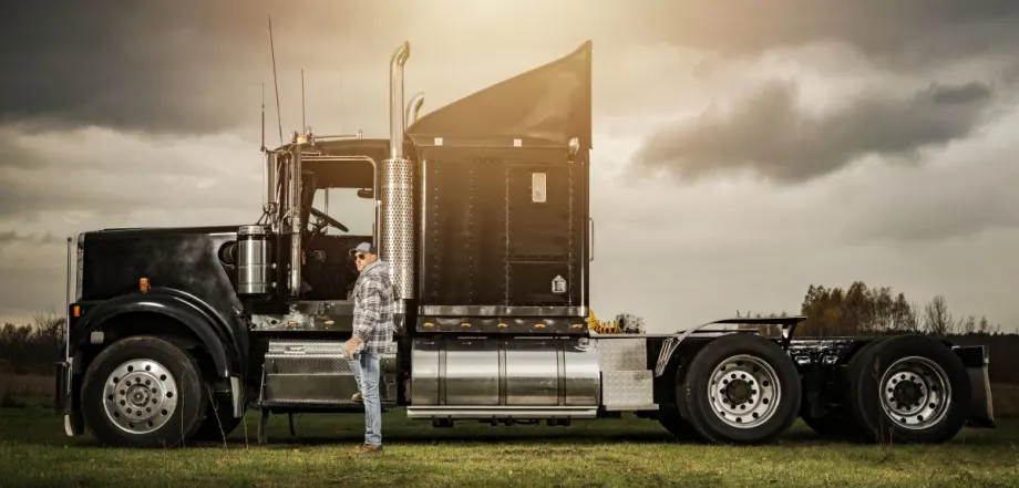 Moody photo of a black classic style commercial truck with a driver standing beside it.