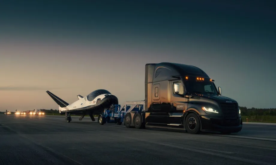 A Freightliner Cascadia semi-truck towing Sierra Space’s Dream Chaser spaceplane on a runway at dusk.