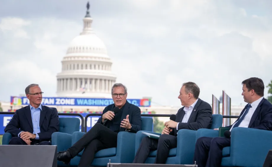 Four men in suits on the National Mall with giant video screen showing capitol building in the background