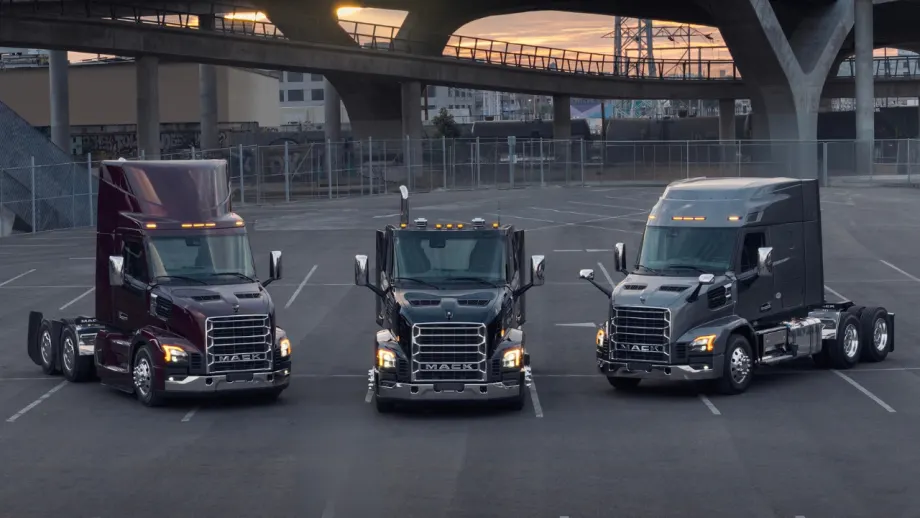 Three Mack Anthem heavy-duty trucks parked side by side beneath an overpass, including two highway tractors and a vocational truck.