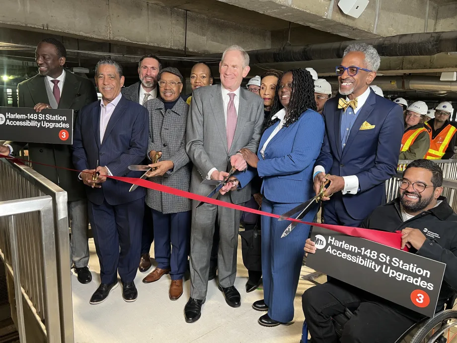 A group of people stand in the Harlem-148 Street 3 Station and pose during a ribbon cutting ceremony.