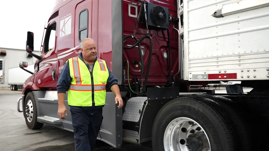 Photo of truck driver in yellow safety vest walking alongside tractor-trailer