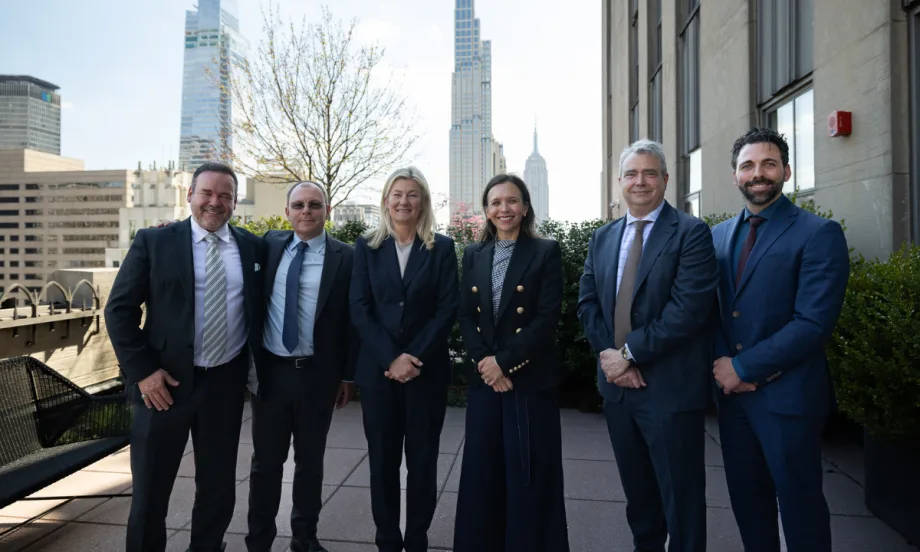 Six people in business wear pose for a picture in front of the Empire State Building in the distance.