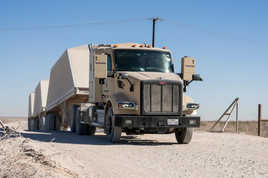 Khaki-colored autonomous Peterbilt truck hauling triple trailers loaded with frac sand for Atlas Energy Solutions in the Permian Basin.