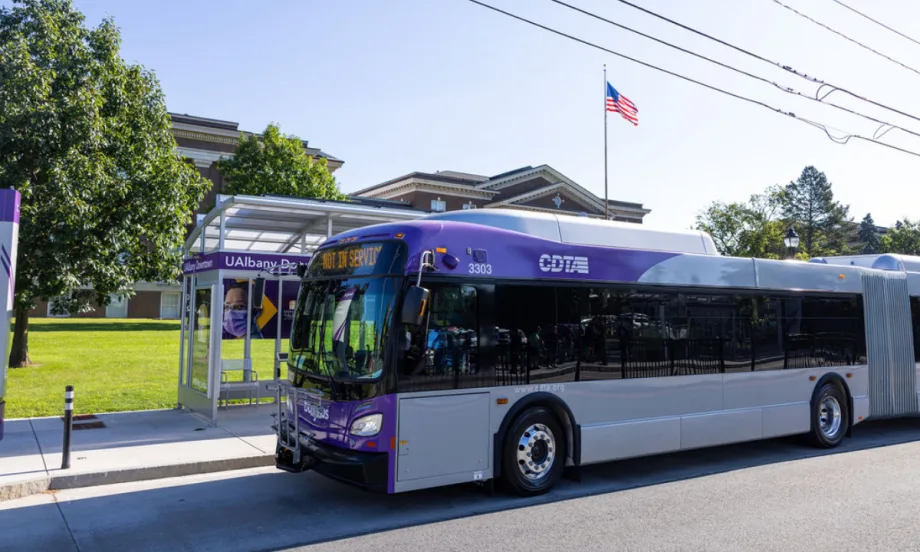 A purple and white CDTA bus parked at a bus stop.