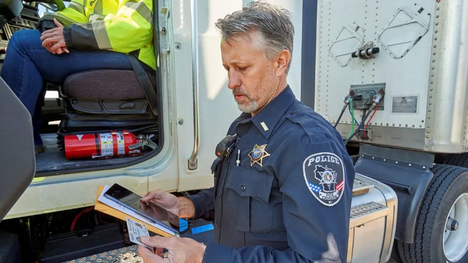 Man with police badge on his arm by an open commercial truck door examining paperwork