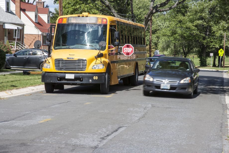 photo of a black sedan passes a stopped school bus with its sign out on a roadway