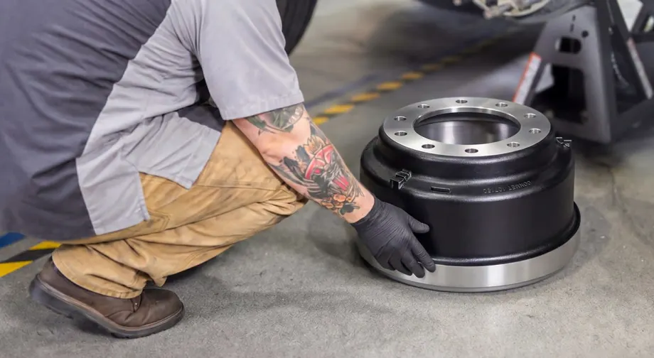 Heavy duty truck technician crouched down replacing brake drum