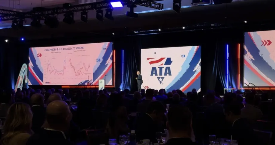 Man on large stage with American Trucking Associations logo in the background and large screen displays of distillate stocks.