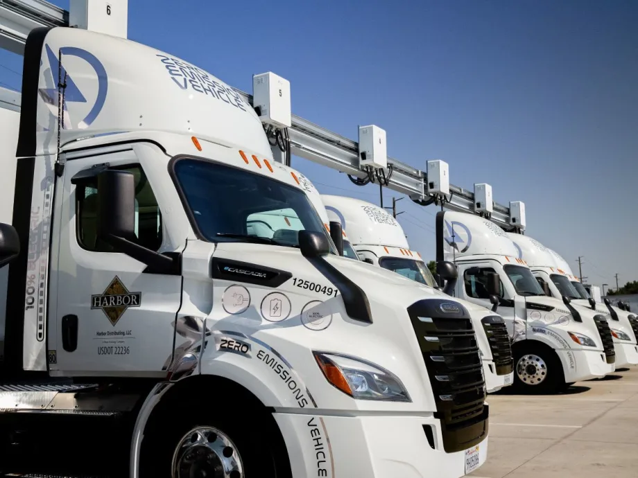 Electric semi trucks parked at a charging station with overhead charging equipment, representing challenges in heavy-duty EV infrastructure deployment.