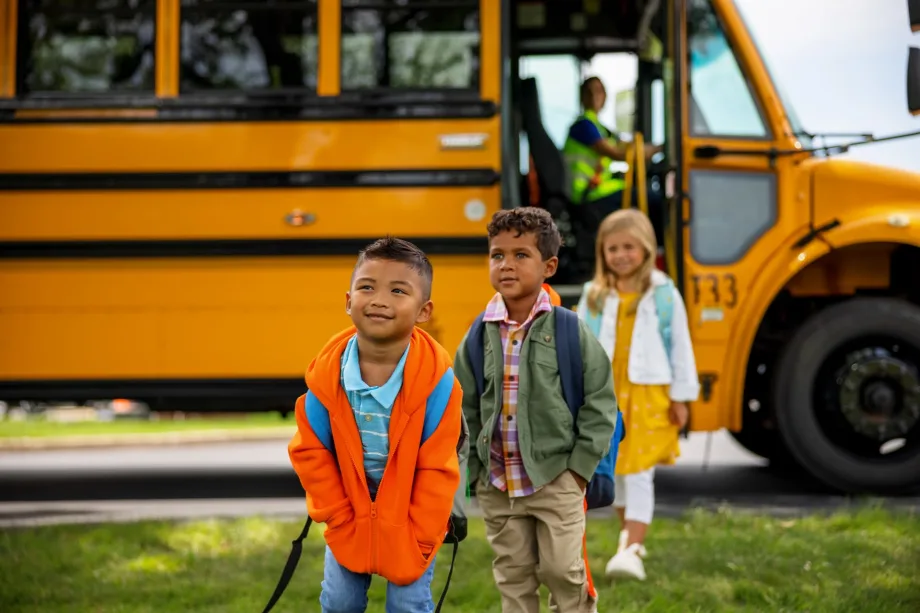 Students walking away from a school bus with a driver in the background, representing efforts to improve student behavior support and safety in school transportation programs.