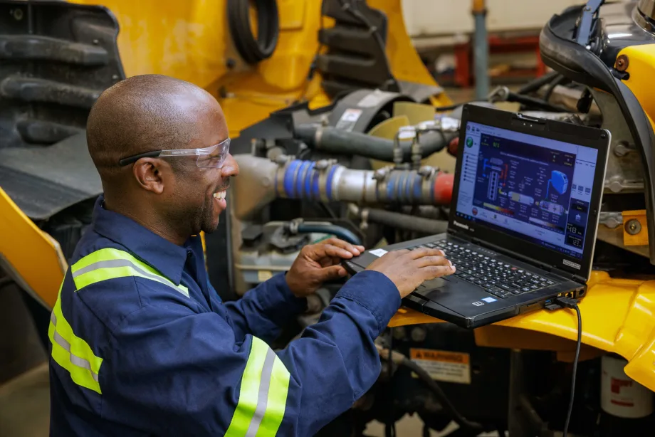 Technician using a laptop to diagnose and service a school bus engine, highlighting fleet maintenance technology and transportation operations.