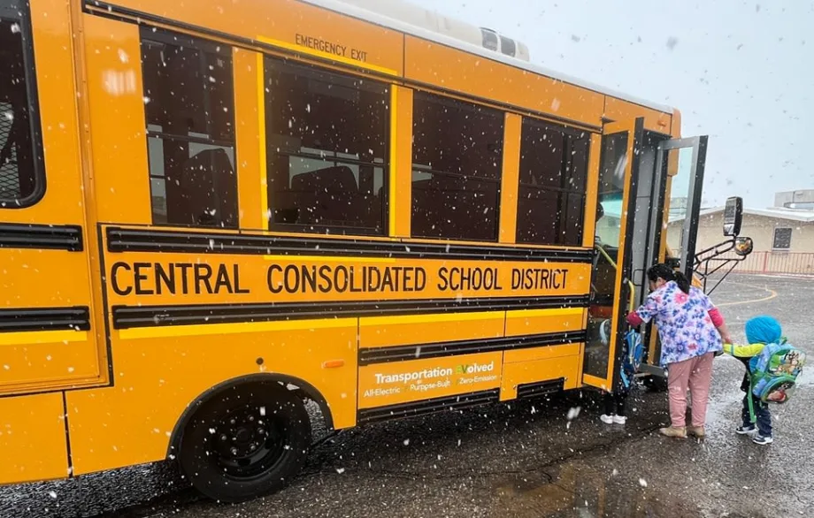 Children board a yellow electric school bus from Central Consolidated School District during snowfall, as an adult assists students at the bus entrance.