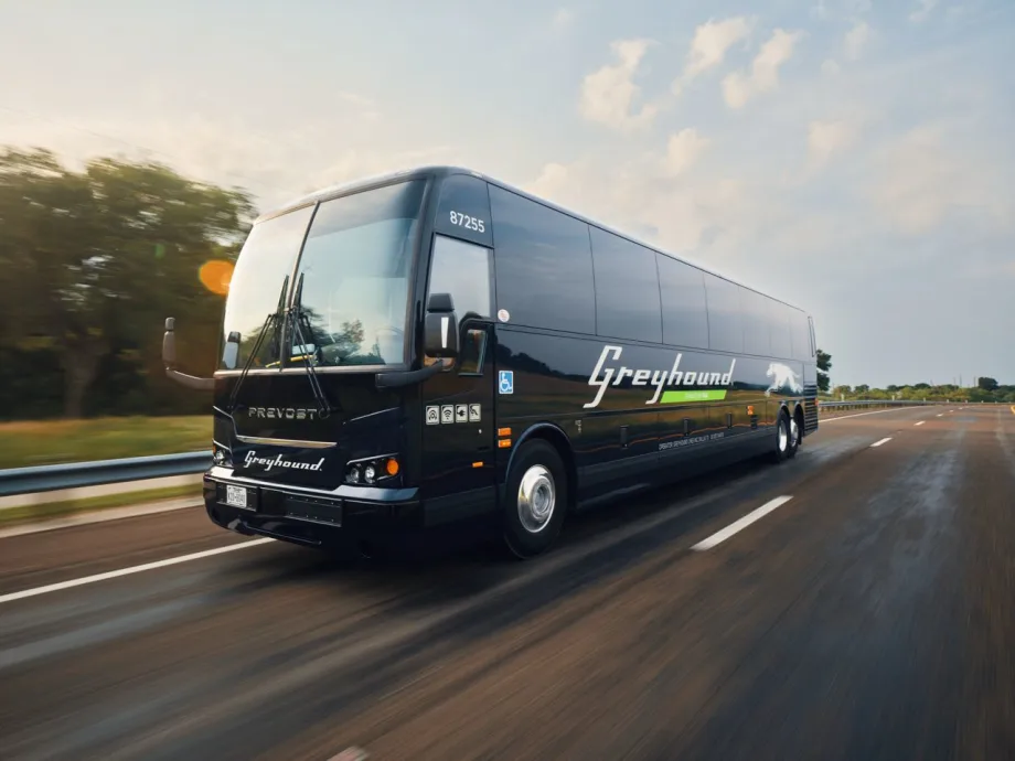 A Greyhound motorcoach driving down a desolate road.