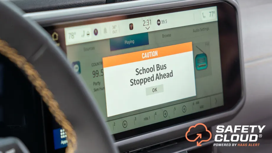 Vehicle dashboard display showing a “Caution: School Bus Stopped Ahead” warning from HAAS Alert’s Safety Cloud system, designed to alert motorists to stopped school buses.