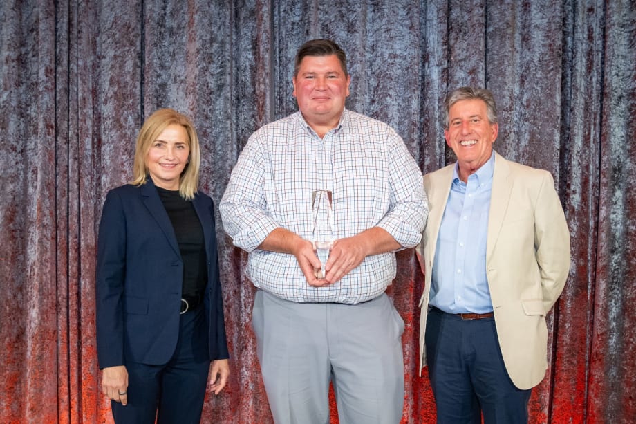 A photo of three people holding a trophy on a stage