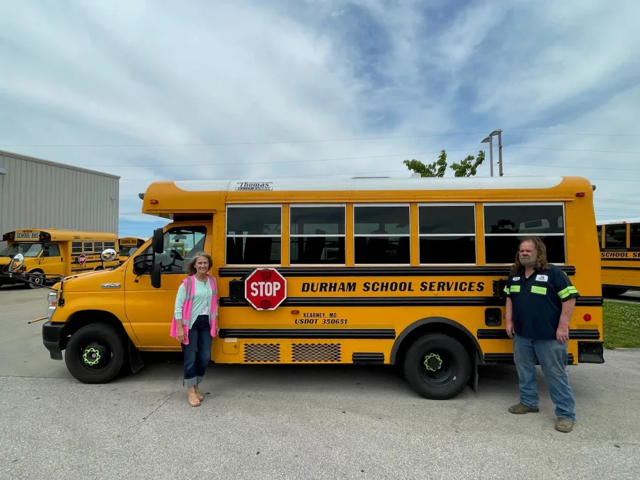A Durham School Services bus with two people posing in front of it.