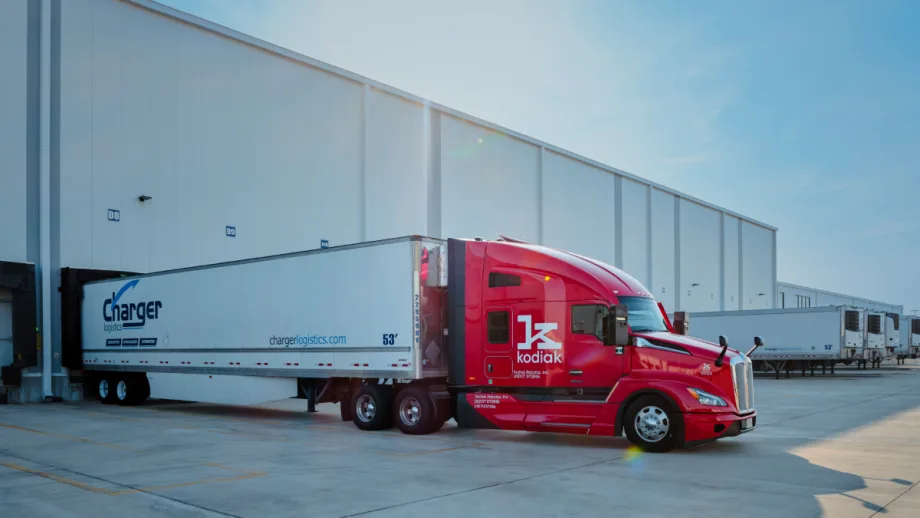 Red Kodiak-branded autonomous tractor with Charger-branded trailer backed up to warehouse