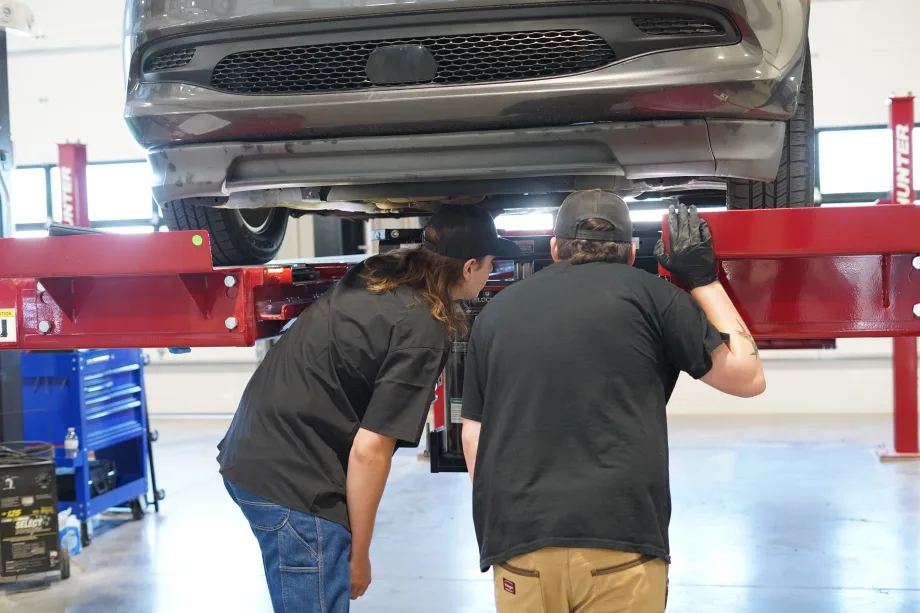 Maintenance officials examining a vehicle on a lift.