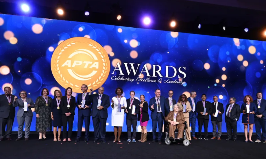 A group of 2026 APTA Award recipients pose onstage with medals and trophies in front of a large APTA Awards backdrop during the awards ceremony.