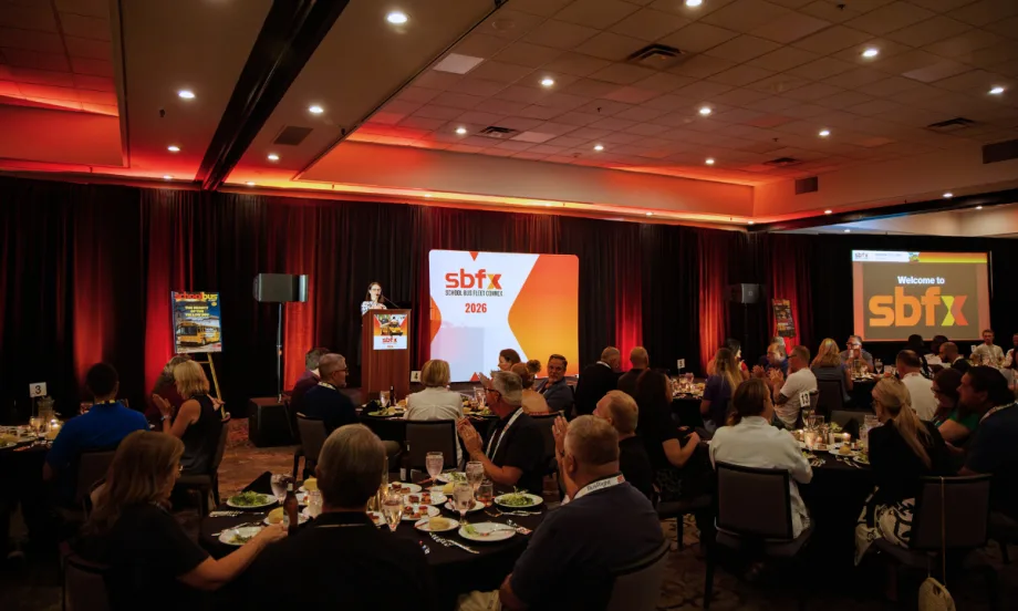 Attendees seated at banquet tables during a School Bus Fleet ConneX 2026 event, with a speaker at the podium and SBFX signage onstage.