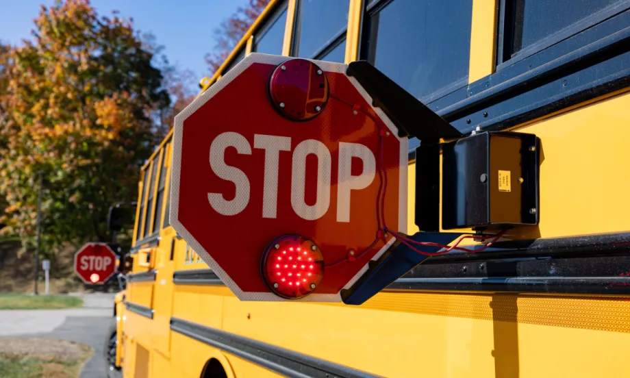 Close-up of an extended red stop arm with flashing lights on the side of a yellow school bus.