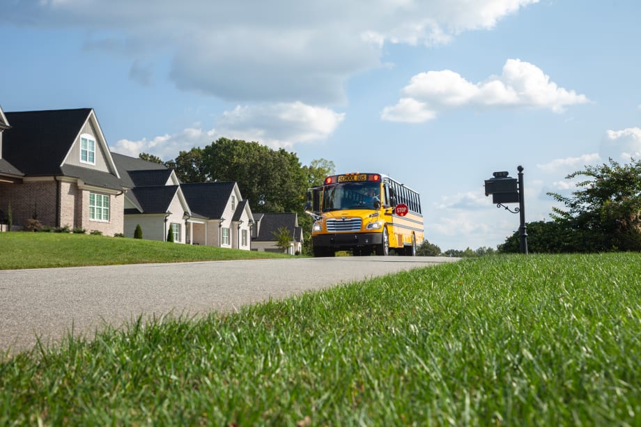 a photo of a school bus driving down a suburban street with houses in the background and green grass pictured