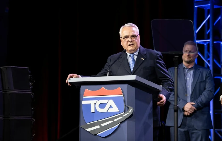 Older white man in suit standing at podium with TCA logo