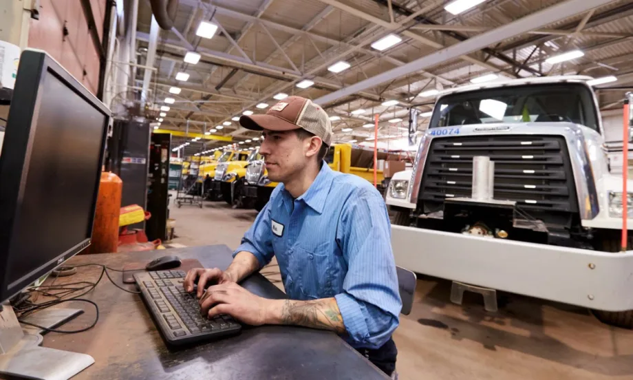 Technician at computer in maintenance shop with truck in background