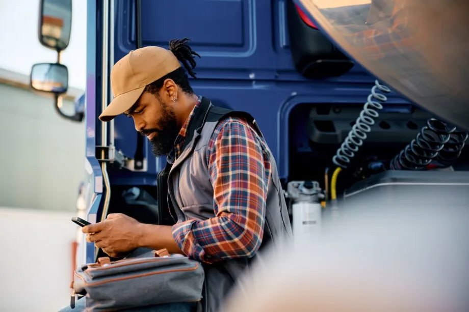 Male truck driver in flannel shirt by truck using his smartphone