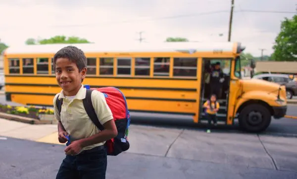 a child walks on the sidewalk with a school bus behind him