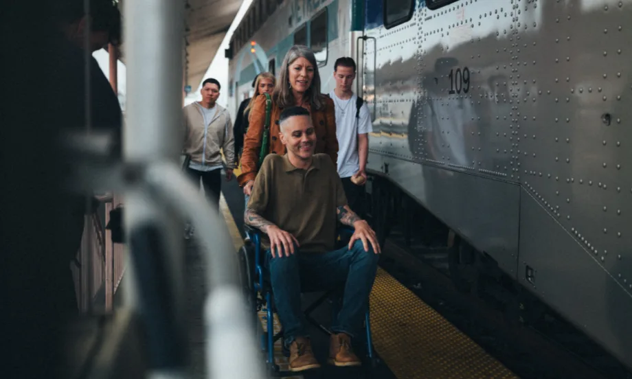 A woman pushes a man in a wheelchair on a rail platform.