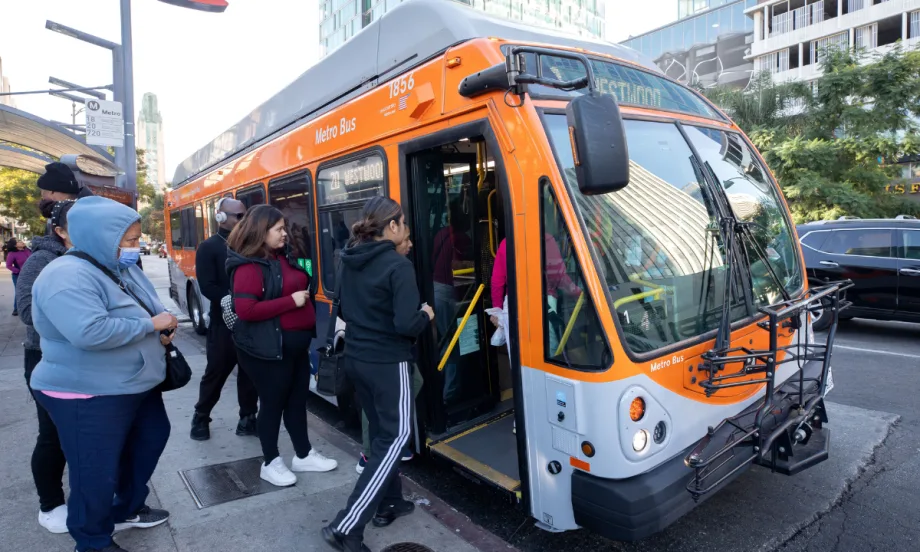 Passengers boarding an orange LA Metro public transit bus.