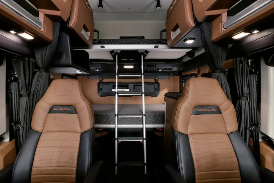 Interior view of the Mack Pioneer sleeper cab, showing two leather seats, an upper bunk with a ladder, overhead storage compartments, and integrated lighting.