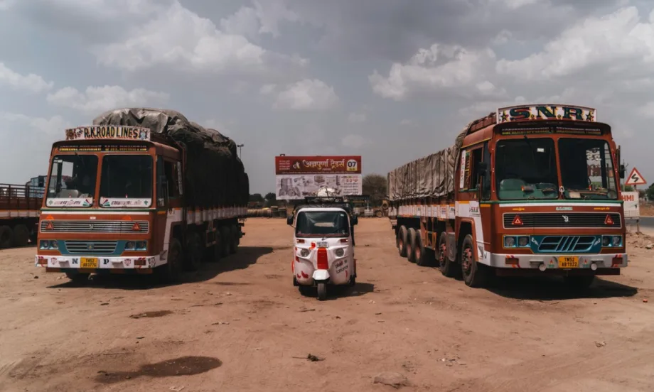 A rickshaw parked between two red transit buses in India.