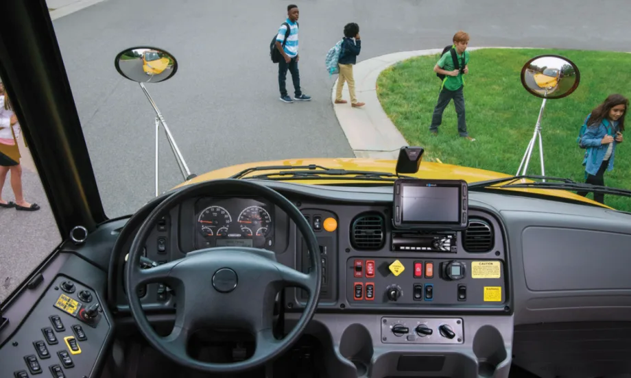 Inside view of a bus driver seat with students walking across the road.