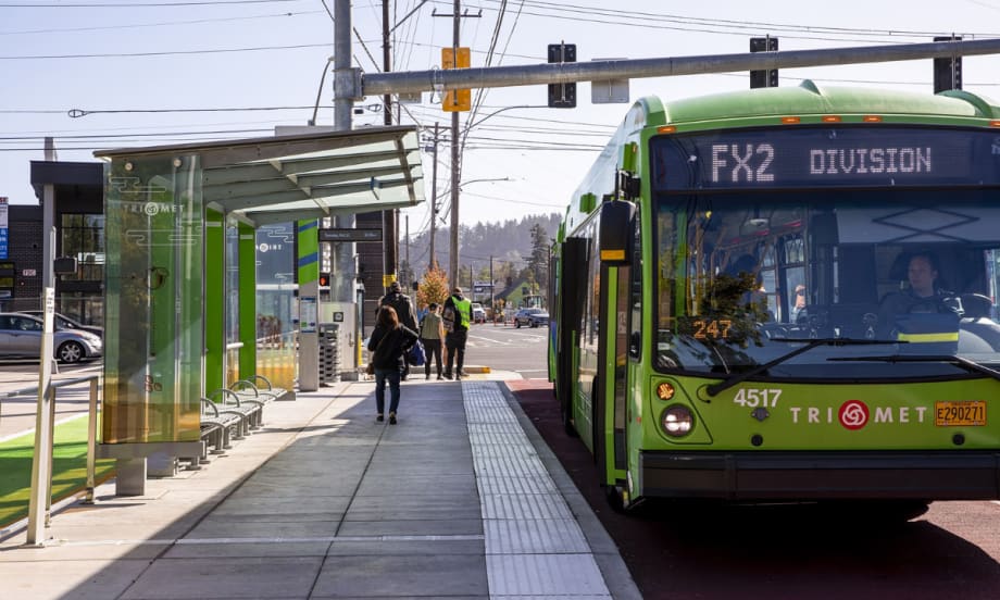 A green TriMet FX bus at a bus stop.