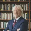 a man in a blue suit stands in front of a bookcase